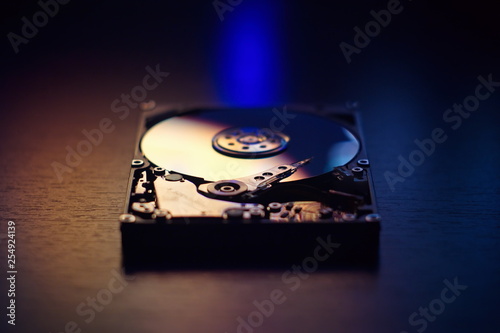 Open / disassembled hard disk on the table in dark colors and lights close-up. Selective soft focus.