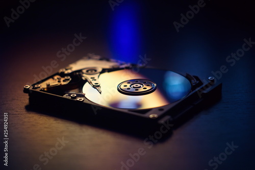 Open / disassembled hard disk on the table in dark colors and lights close-up. Selective soft focus.