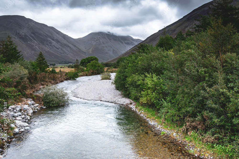 Stream in beautiful, green valley and moody sky above mountain peaks. Stream in beautiful, green valley and moody sky above mountain peaks.