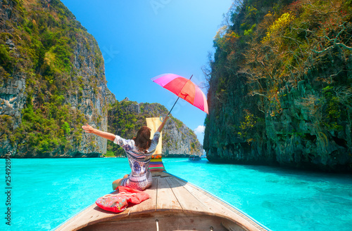Joyful woman with umbrella travels in summer clothes on a boat among the islands of Phi Phi in Thailand