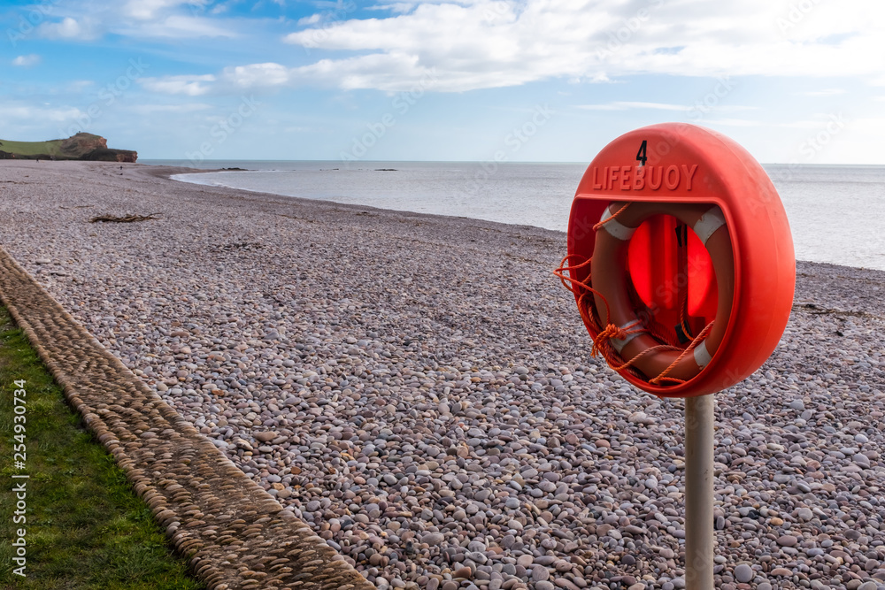 An orange lifebouy on a deserted Budleigh Salteron Beach, Devon, UK. The beach is made up of pebbles.
