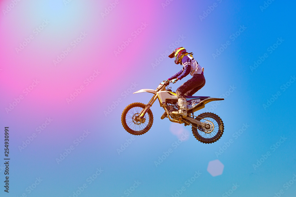 Extreme sports background - silhouette of biker jumping on motorbike on sunset, against the blue sky
