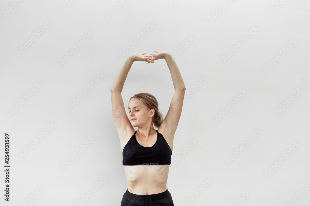 Girl in a sporty black top and shorts on a light background stretches to the up Girl in a sporty black top and shorts on a light background stretches to the up