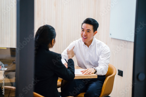 A youthful Asian Chinese expert is giving an introduction before his partner in the workplace. He is very happy with the discussion and looking extremely brilliant in his office clothing.