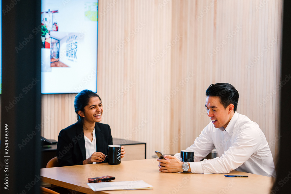 Teammate talking to each other while enjoying their coffee. They are discussing work-related stuff inside a conference room and looking good in their office attire.