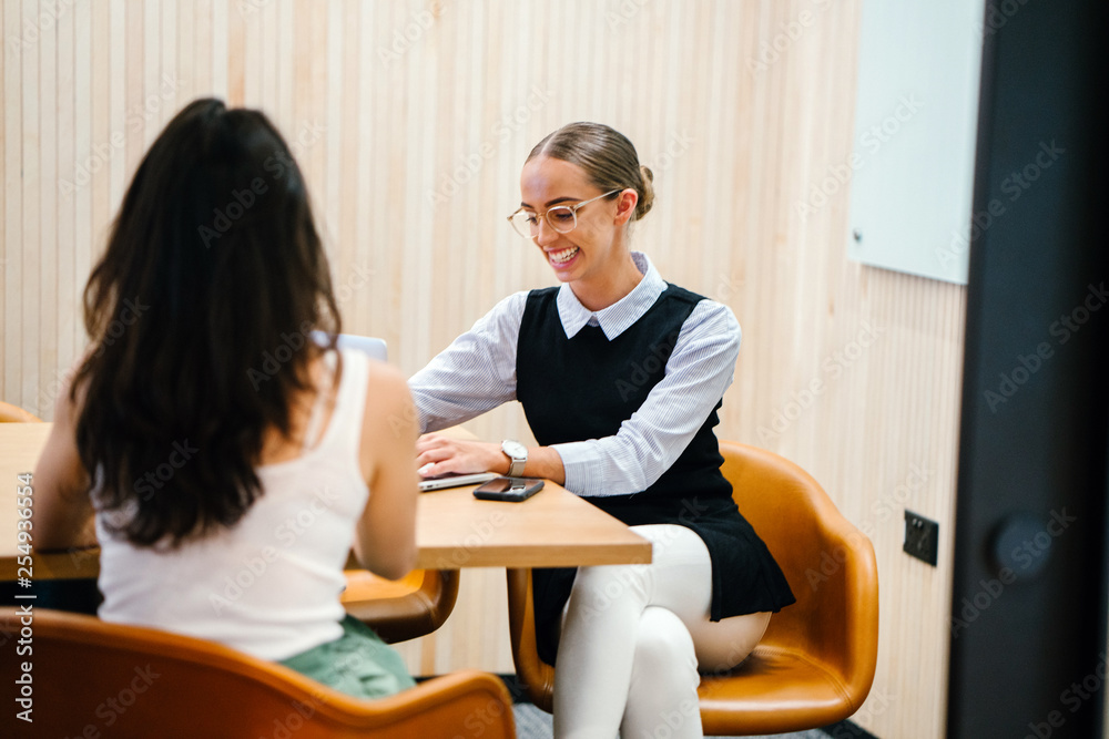 A Caucasian woman talking to a teammate inside the conference room. She is discussing some work while sitting down on a desk and looking beautiful in a black dress. A Caucasian woman talking to a teammate inside the conference room. She is discussing some work while sitting down on a desk and looking beautiful in a black dress.