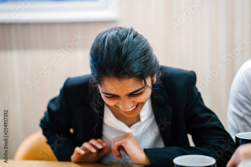 Portrait of an attractive,confident middle-aged Asian woman (Indian) professionally dressed and is laughing while having a discussion with her officemates whose out of view in the office. photo