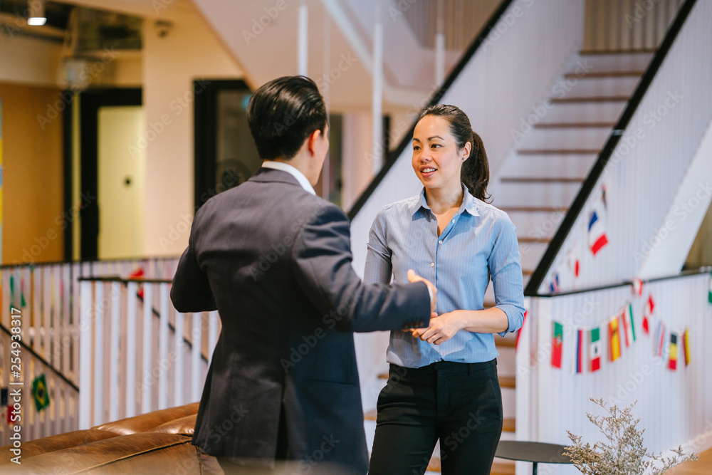 Portrait of two Asian Chinese business people in a corporate attire having a casual discussion in the office pantry during the day. Image taken with a blur stair as background. Portrait of two Asian Chinese business people in a corporate attire having a casual discussion in the office pantry during the day. Image taken with a blur stair as background.