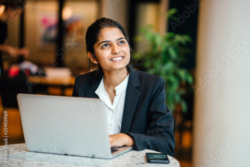 A beautiful Indian woman admiring a teammate while in a discussion. She is smiling in front of a colleague while working on a laptop. 
