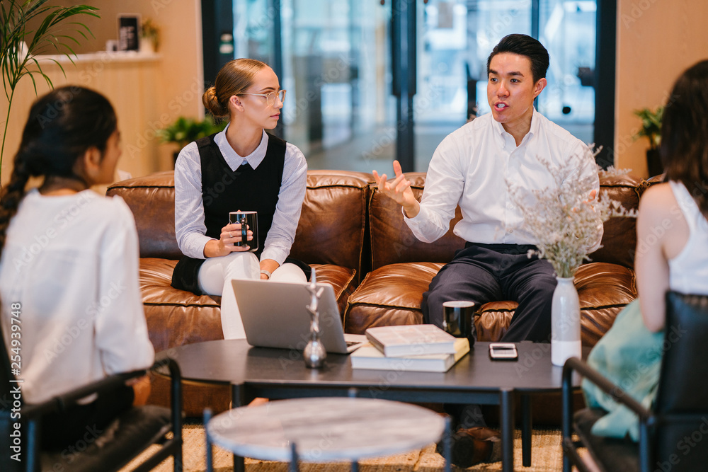 A group of professionals discussing work inside the office. They are wearing elegant corporate attire while sitting on a brown couch. 