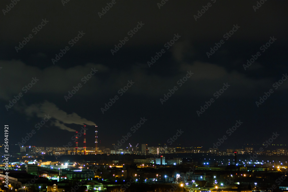 City skyline at night.Night view of a neighbourhood with low-rise apartment blocks illuminated window lights. Pipes of thermal power plant smoke