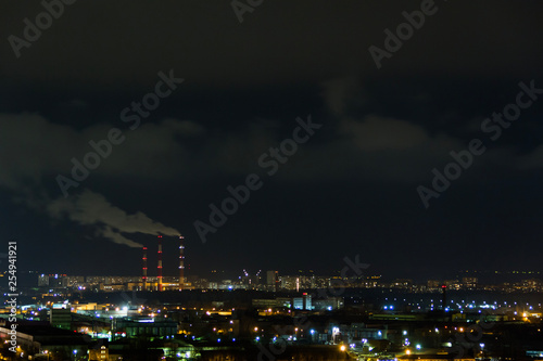 City skyline at night.Night view of a neighbourhood with low-rise apartment blocks illuminated window lights. Pipes of thermal power plant smoke © GMars