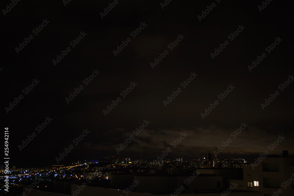 Night city skyline. Top aerial panoramic view of modern city from tower rooftop. Road junction traffic. Heavy clouds on the dark sky