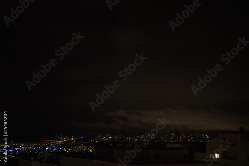Night city skyline. Top aerial panoramic view of modern city from tower rooftop. Road junction traffic. Heavy clouds on the dark sky