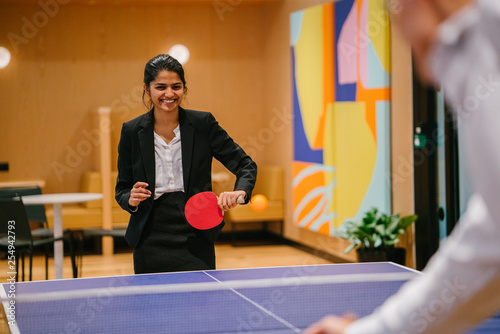 Canvas Print Portrait of a young and attractive Indian Asian woman in a suit playing table tennis with her colleague in the office during a break