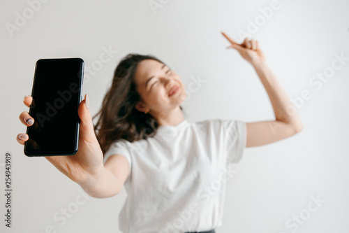 Portrait of a confident casual asian girl showing blank screen of mobile phone isolated over gray background at studio.