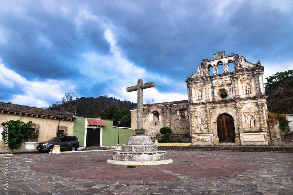 Church fassade ruin of Ermita de Santa Isabel and cross on plaza with dramatic cloudscape, Antigua, Guatemala