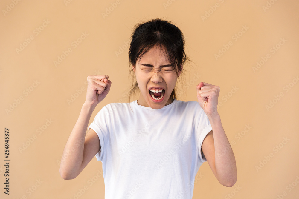 Photo of emotional korean woman wearing basic t-shirt smiling and clenching fists Photo of emotional korean woman wearing basic t-shirt smiling and clenching fists