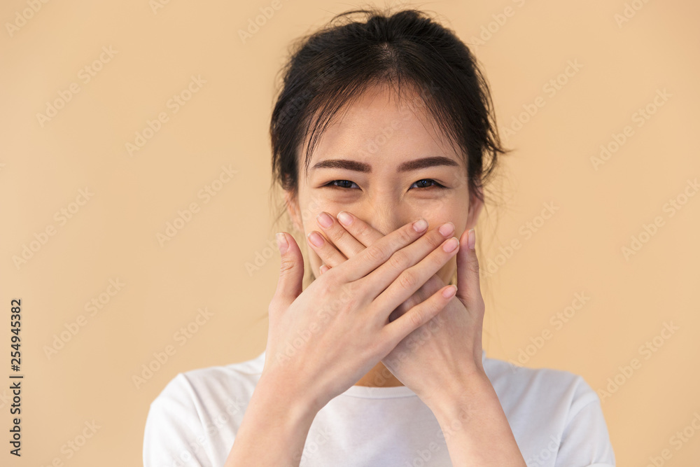 Image of joyous chinese woman wearing basic t-shirt covering her mouth with hands Image of joyous chinese woman wearing basic t-shirt covering her mouth with hands