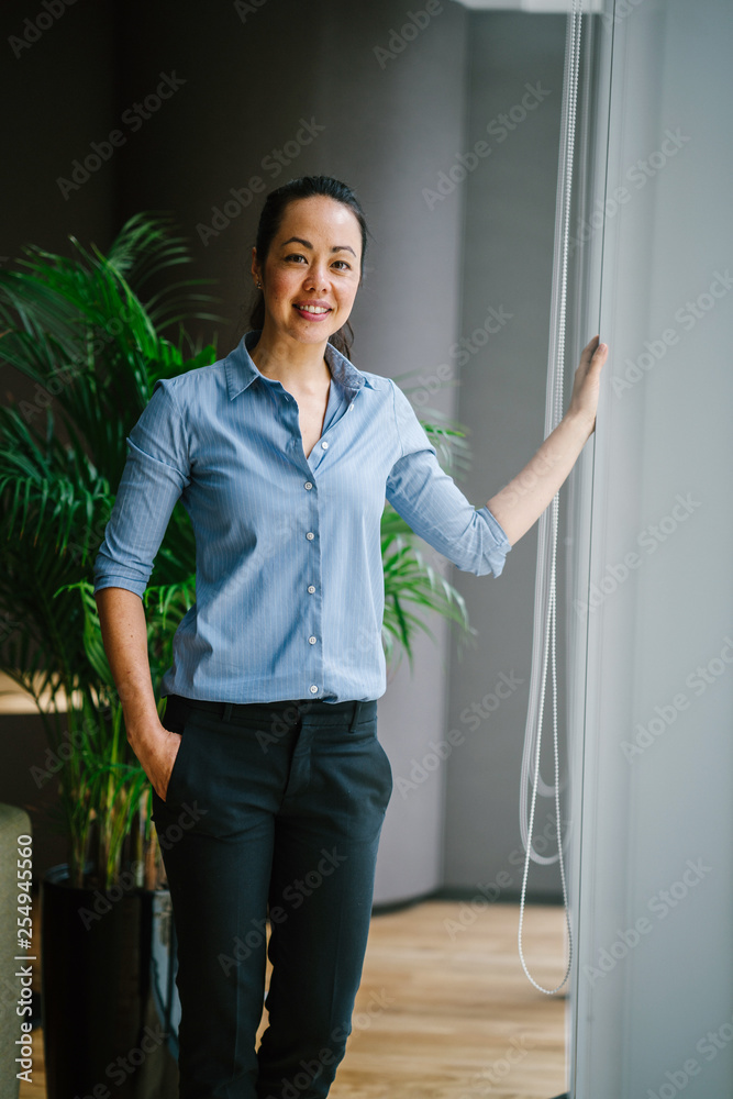 Portrait of a lovely businesswoman standing next to a glass window in the conference centre. She wears black pants with a blue shirt that makes her look so professional and competent. Portrait of a lovely businesswoman standing next to a glass window in the conference centre. She wears black pants with a blue shirt that makes her look so professional and competent.