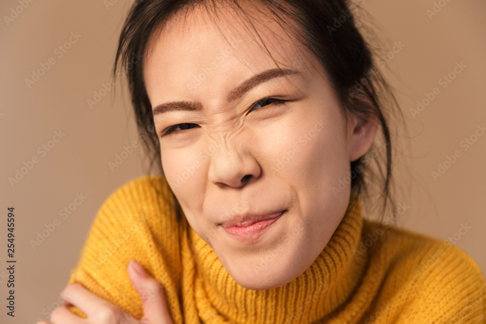 Image closeup of funny asian woman wearing sweater grimacing while posing at camera in studio Image closeup of funny asian woman wearing sweater grimacing while posing at camera in studio