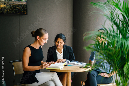A young Indian Asian woman is having a business meeting with her team in a meeting room. She is smiling as she talks to her colleagues. They are all professionally dressed.