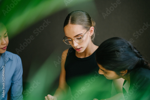 A young Caucasian woman has a casual business meeting with her team. They're sitting down and talking in depth. One of her team mate is Chinese while the other is Indian.