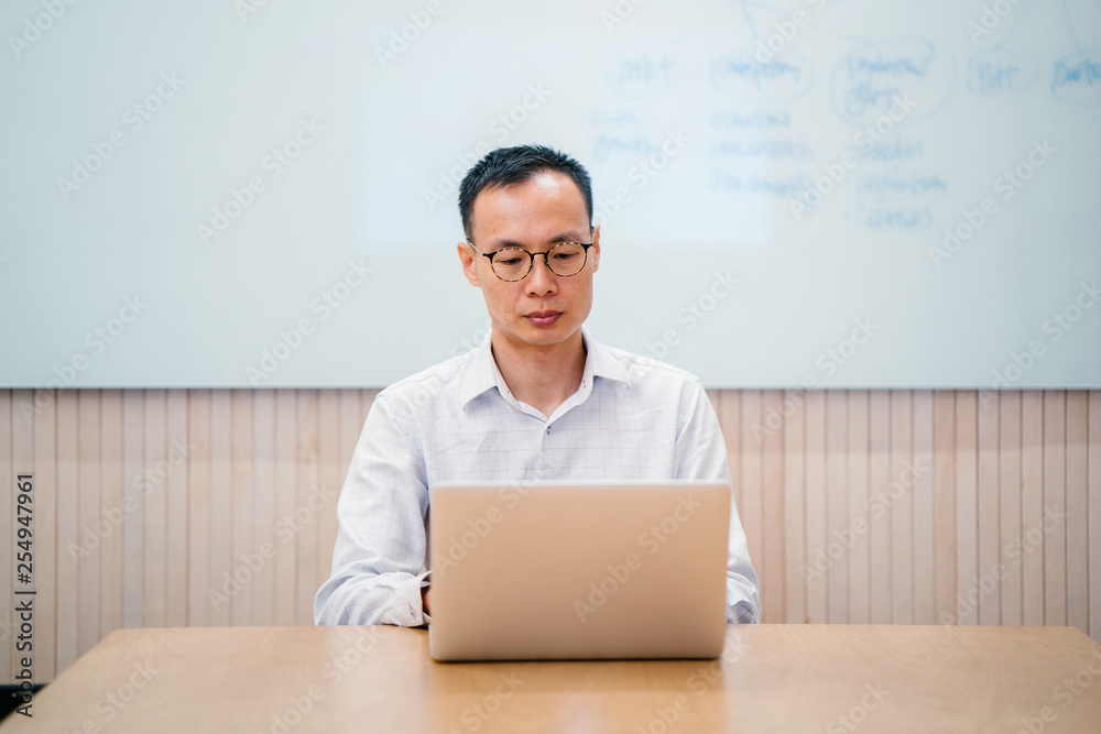 Image of a confident and attractive Asian businessman sitting and working on his task on his computer. He is wearing a simple outfit, but still looks good and knowledgeable. Image of a confident and attractive Asian businessman sitting and working on his task on his computer. He is wearing a simple outfit, but still looks good and knowledgeable.
