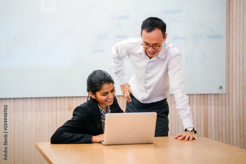 A Chinese businessman is having a discussion with an Indian colleague inside a meeting room. They are focused on the laptop in front of them. A Chinese businessman is having a discussion with an Indian colleague inside a meeting room. They are focused on the laptop in front of them.