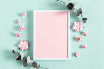 Flowers composition creative. Blank photo frame, pink flowers, eucalyptus branches on pastel mint background. Flat lay, top view, copy space