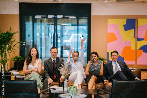 Portrait of a happy business group sitting on a couch in their office. All are dressed professionally and are doing a wacky pose to the camera.