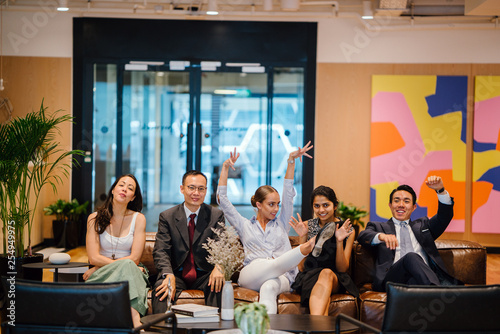 Portrait of a happy business group sitting together on a couch in their office. They're all dressed professionally and making a wacky pose for the camera.
