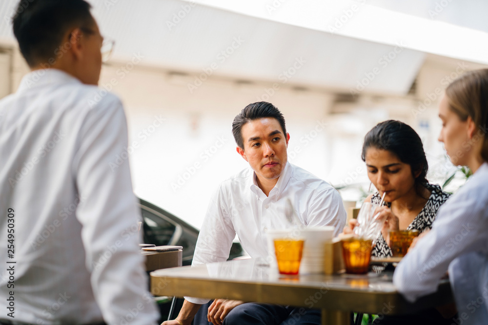 A group of young business people is sitting outside a cafe having a meeting during the day.