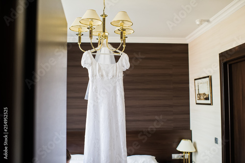 Elegant wedding dress hanging on the chandelier in the interior of the hotel