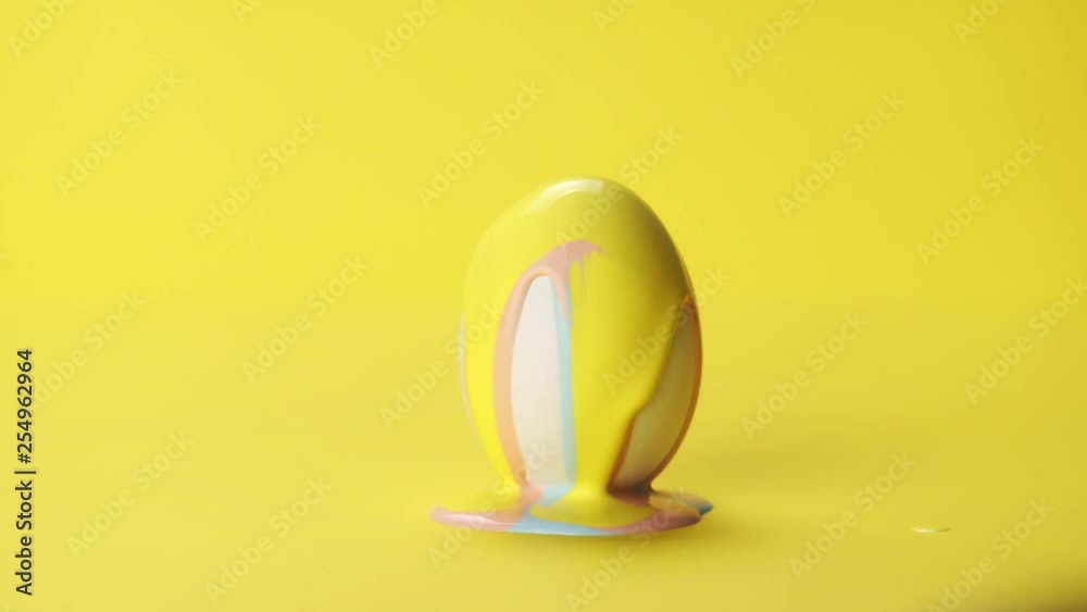 Yellow and pink color paint slow flowing on white egg on yellow background, colors mixing together. Concept Easter painted eggs, party, celebration Yellow and pink color paint slow flowing on white egg on yellow background, colors mixing together. Concept Easter painted eggs, party, celebration
