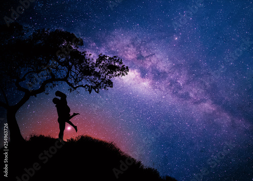 Milky Way with couple  under the tree on the hill. Landscape with night starry sky and silhouette of standing happy man and woman hugging in starry sky. Milky way with travelers,copy space. photo