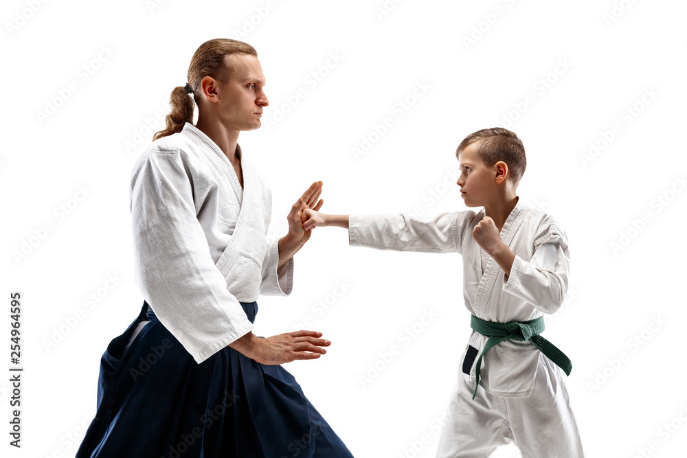 Man and teen boy fighting at Aikido training in martial arts school. Healthy lifestyle and sports concept. Fightrers in white kimono on white background. Karate men with concentrated faces in uniform.