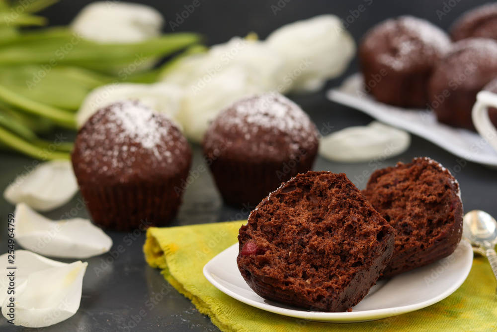 Chocolate muffins with cherry, covered with powder sugar located on a dark background