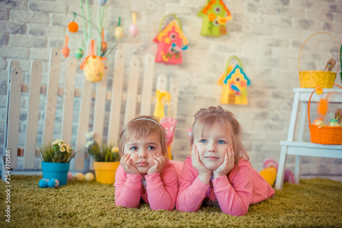 Little cute caucasian cheerful girls in pink dresses in holiday easter decorations at home. Childhood, easter holiday, family concept