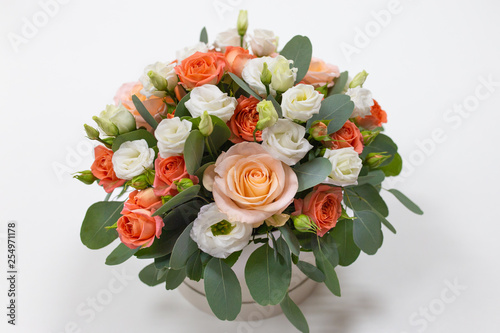 Delicate floral arrangement of roses (white, pink, orange) and green eucalyptus leaves in a round white cardboard box on a light background © Belogen