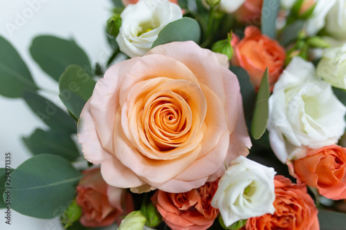 Delicate floral arrangement of roses  white  pink  orange  and green eucalyptus leaves in a round white cardboard box on a light background