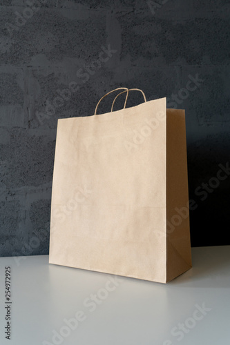 Paper brown shopping bag with free space for text on the white table, symbolizing shopping, purchase, marketing. Side view