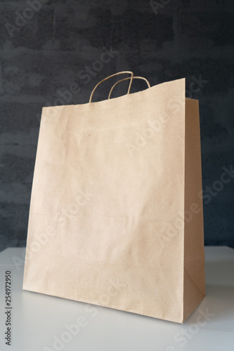 Close-up of paper brown shopping bag with free space for text on the white table, symbolizing shopping, purchase, marketing. Side view