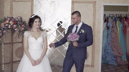 slow motion handsome fiance with purple rose bouquet hugs and kisses pretty bride against mirror