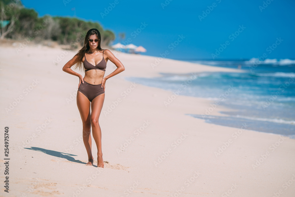 Beautiful tanned girl posing on beach with white sand and blue ocean.