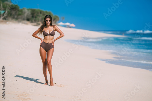 Beautiful tanned girl posing on beach with white sand and blue ocean.