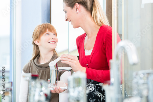 Happy mother looking with her daughter at two faucets in a sanitary ware shop photo