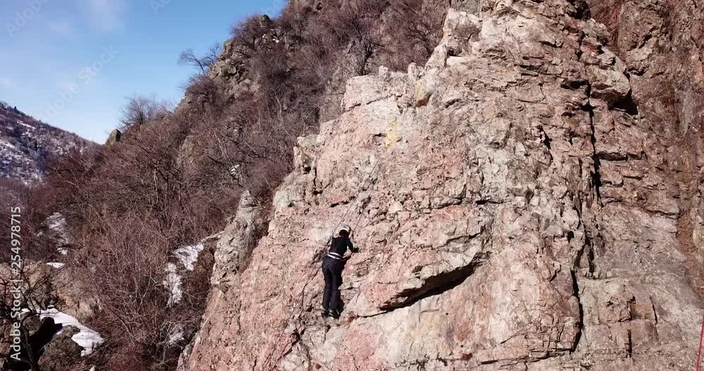 Climber climbs the rock. Girl and boy climb the rock. Rock climbing lessons. Rocky cliff. Winter nature. Drone footage. Extreme sport. A group of people trained climbing. Trees without leaves and gras