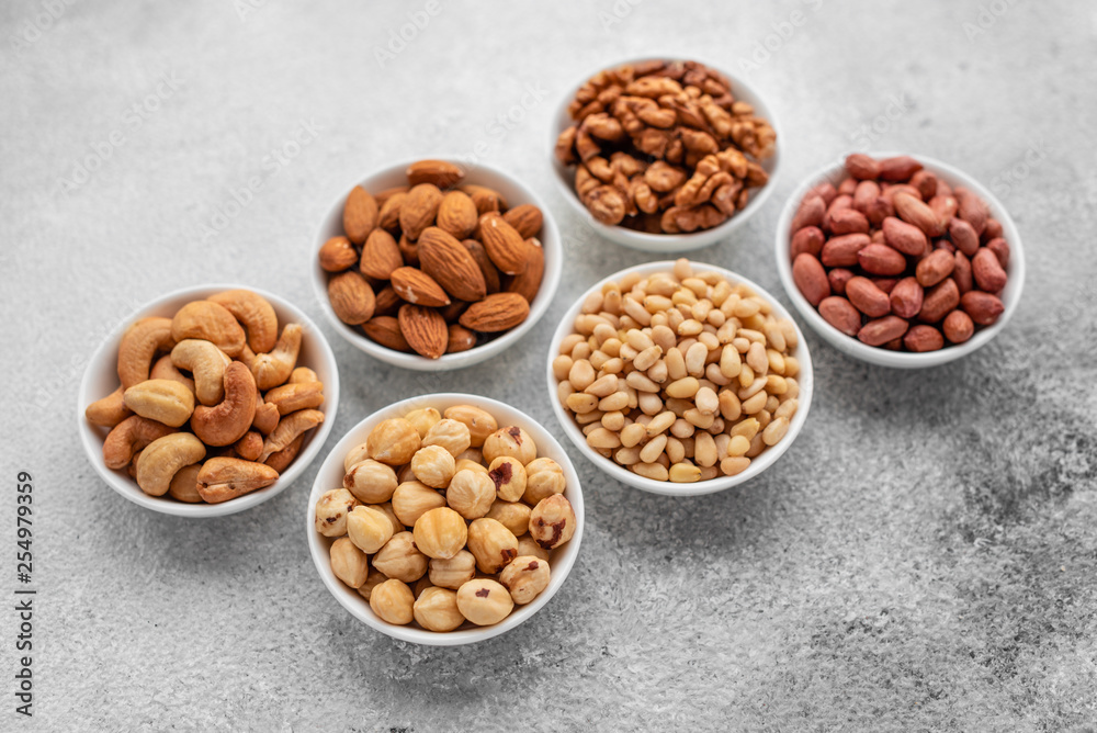 Assortment of nuts in white saucers on a concrete background. Food mix background, top view, copy space, banner Assortment of nuts in white saucers on a concrete background. Food mix background, top view, copy space, banner