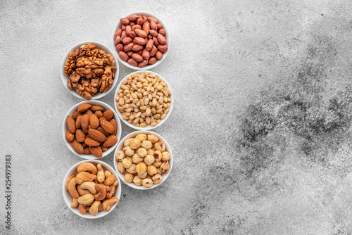 Assortment of nuts in white saucers on a concrete background. Food mix background, top view, copy space, banner